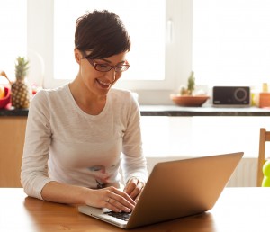 Beautiful young woman with coffee using laptop in the kitchen